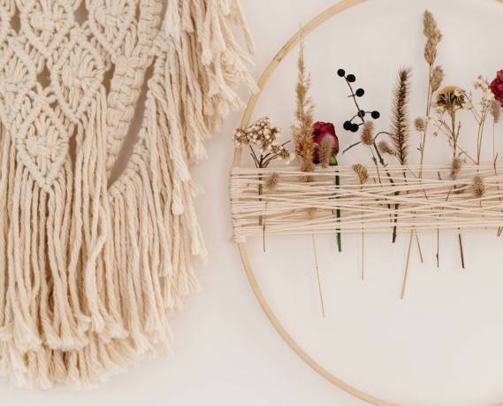 Stylish boho wreath with dry flowers and macrame hanging on white wall. Modern floral arrangement and creative handmade decor in modern boho room